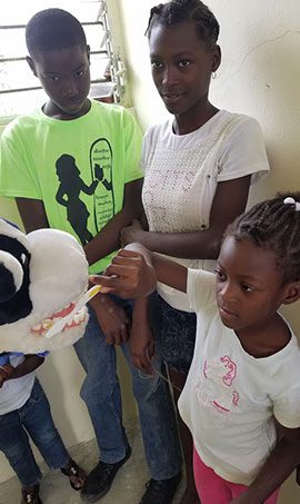 A member of the Georgia Knotek DDS dental team uses a cow puppet to show a younger child how to properly brush teeth