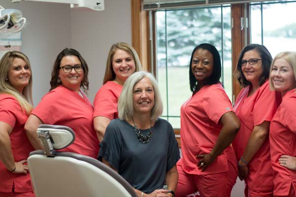 The staff of Georgia Knotek DDS wearing red while Dr. Georgia Knotek wears black and sits on a dental chair at Georgia Knotek DDS in Greenfield, IN