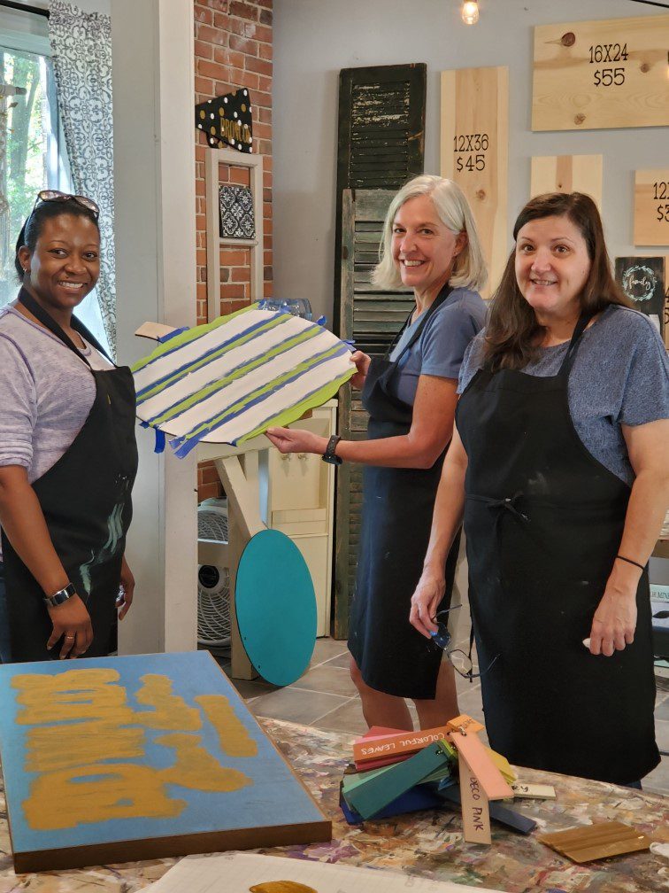 Three members of the Georgia Knotek DDS staff wearing black smocks working on some custom signs at a local art studio in Greenfield, IN