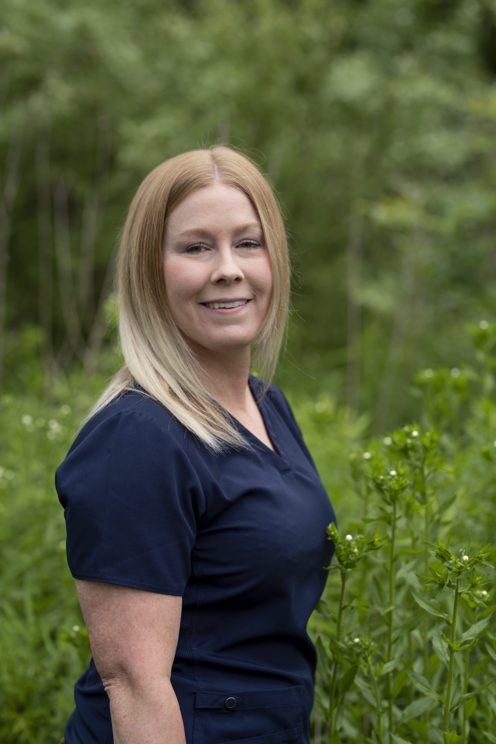 Sabrina, dental assistant, wearing a blue shirt standing in a green forest in Greenfield, IN