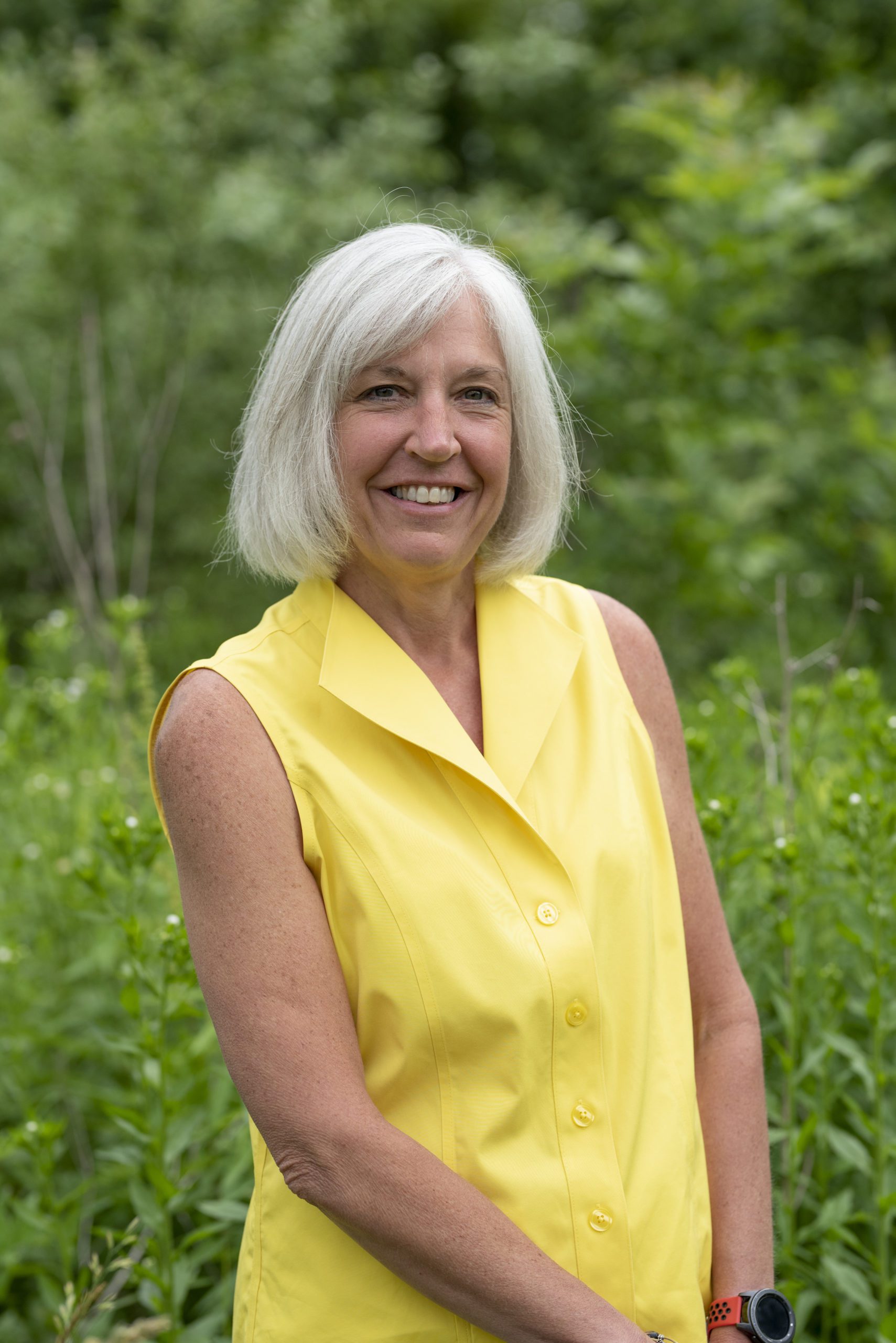 Dr. Georgia Knotek wearing a yellow sleeveless shirt in front of a green forest in Greenfield, IN