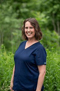 Monica, dental hygienst, wearing a blue shirt in front of a lush forest in Greenfield, IN